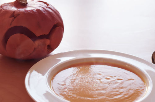 Eine Kürbissuppe im Vordergrund und dahinter ein geschnitzter Halloween Kürbis